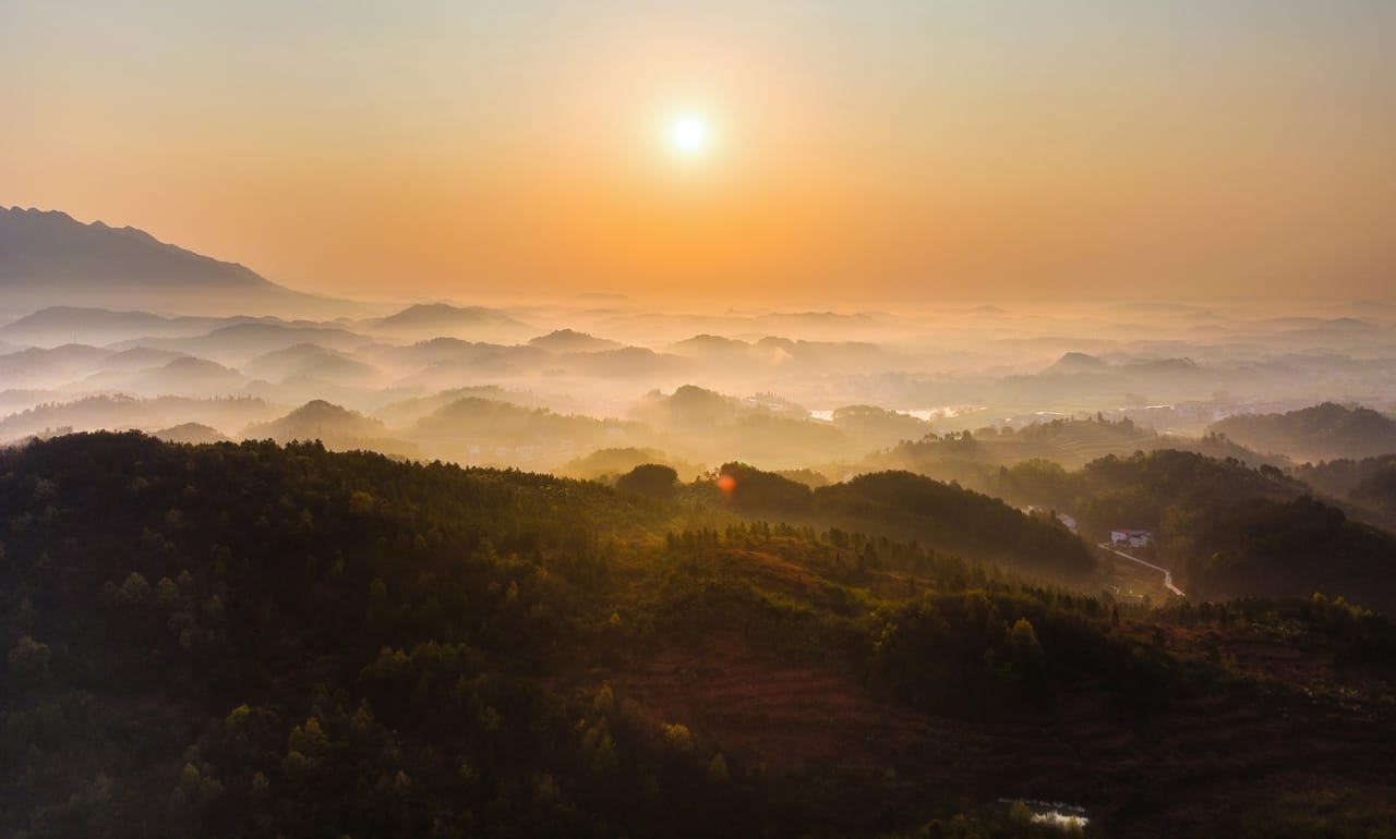 The sun rising over hills in a sea of fog