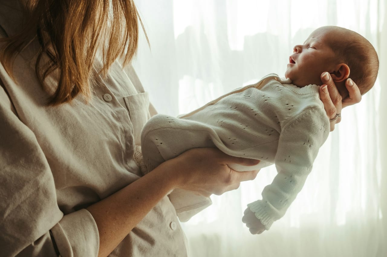 A mother holding her newborn baby by a window